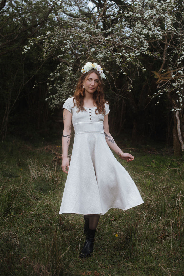 Square neck beige folklore dress with corset back, shown in a woodland setting with a flower crown