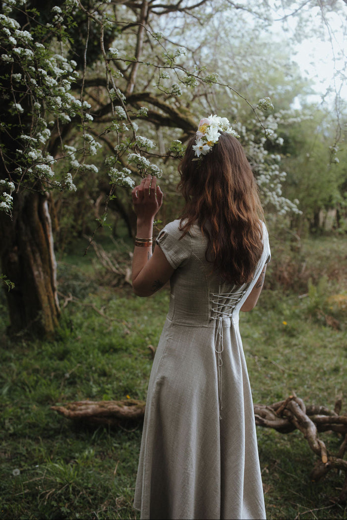 Back view of beige folklore midi dress with corset back, natural fibre dress with a softly flared skirt in woodland scenery