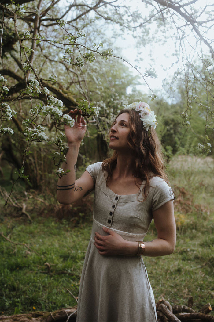 Midi cottagecore natural dress with pockets in soft beige, photographed beneath blossom trees in a romantic forest setting