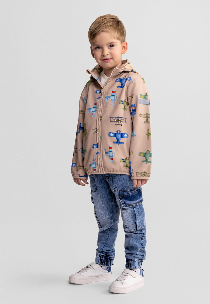 Boys softshell jacket in sand with aeroplane print, front view, features attached hood and zippered pockets.