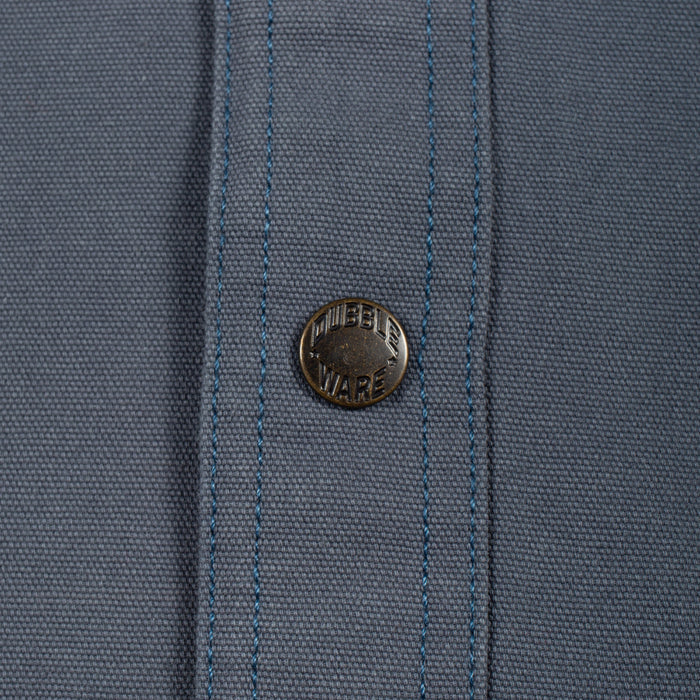 Close-up of a slate blue woven fabric with a single round metal button featuring the 'MURDER WARE' brand name.