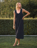 Woman wearing a navy sleeveless dress standing outdoors with greenery in the background