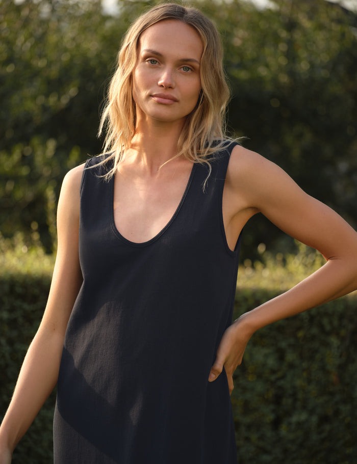 Woman wearing a navy sleeveless dress outdoors with greenery in the background