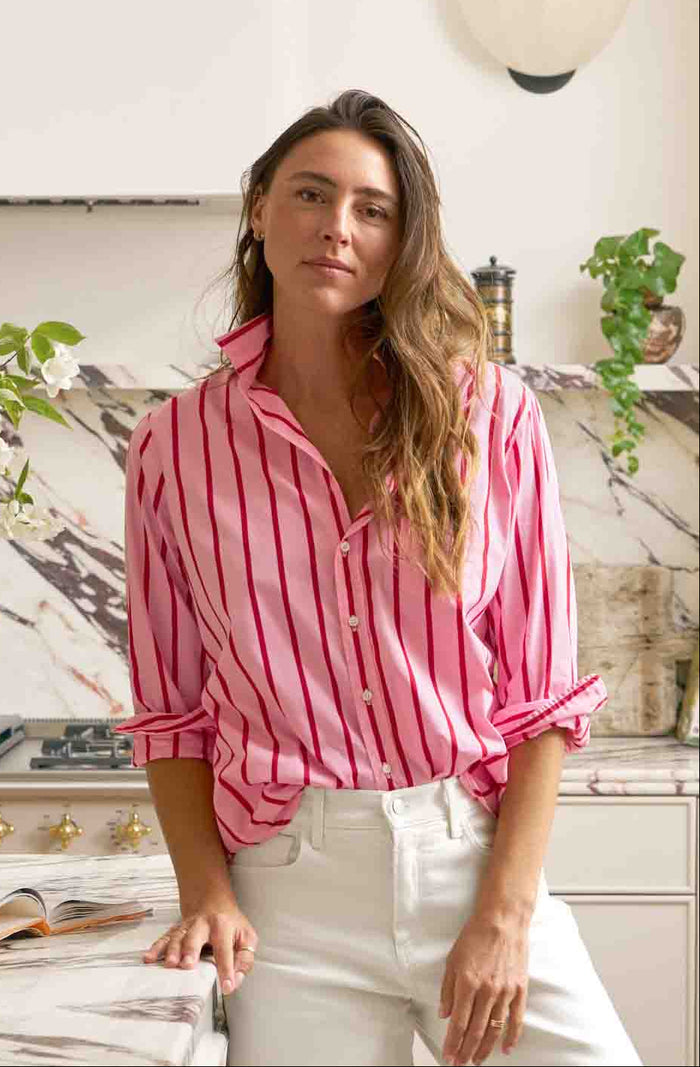 Woman in a pink striped shirt and white pants standing in a modern kitchen.