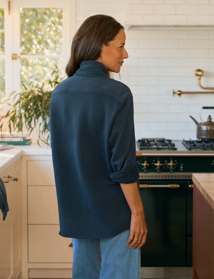 Woman standing in a kitchen wearing a blue shirt and jeans.