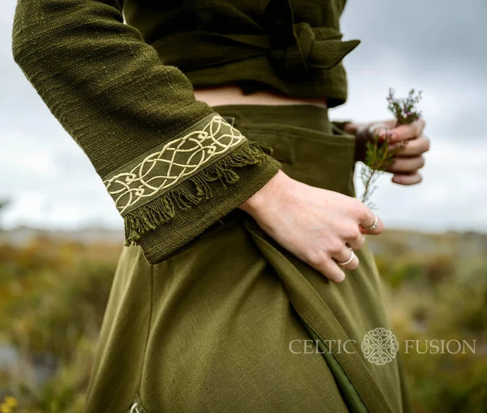 Close-up of the olive green folklore wrap top showing cream Celtic knotwork embroidery and soft fringe on the flared cuff.