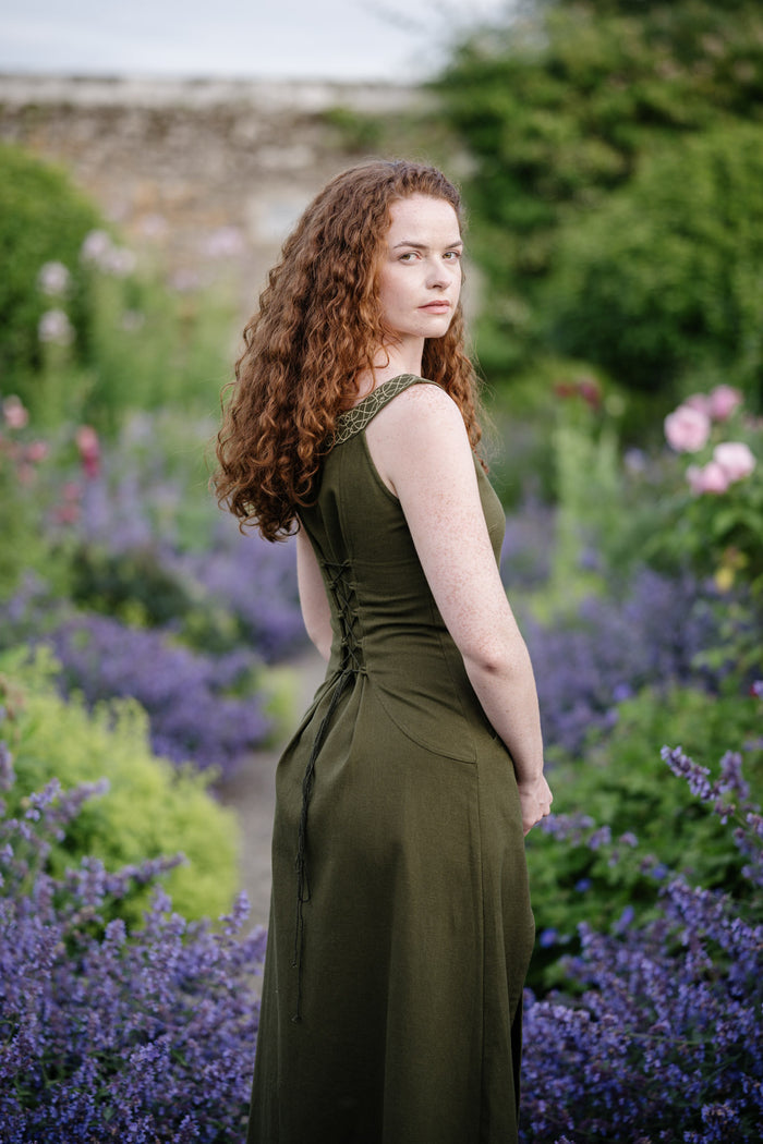 Forest green sleeveless folklore dress with Celtic embroidered neckline and front slit, photographed in a natural setting