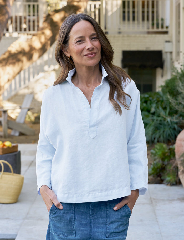 Woman wearing a blue shirt and blue skirt standing outdoors near a pool.