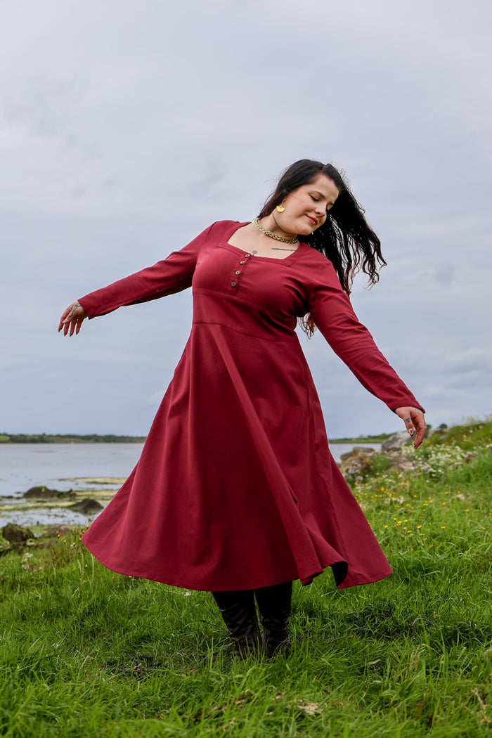 Berry red Imbas Corset Dress outdoors by the coast, long sleeve folklore midi dress with fitted bodice and flowing skirt