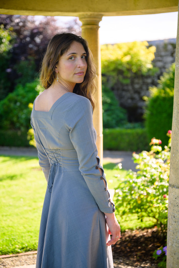 Pastel blue sleeved dress showing the adjustable corset lace-up back and decorative buttoned sleeve openings.
