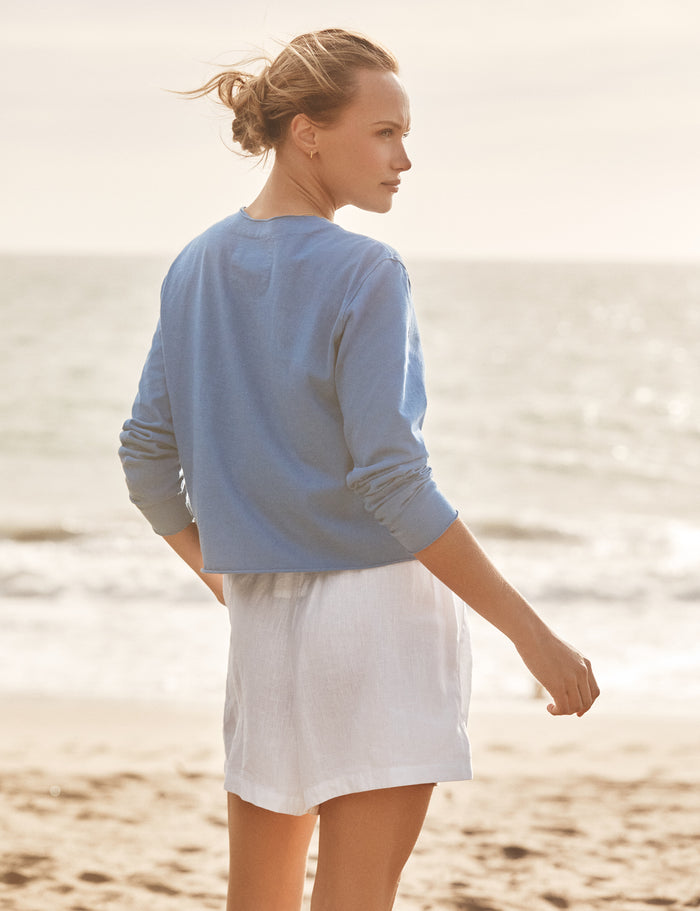 Woman in a blue sweater and white skirt standing on a beach.