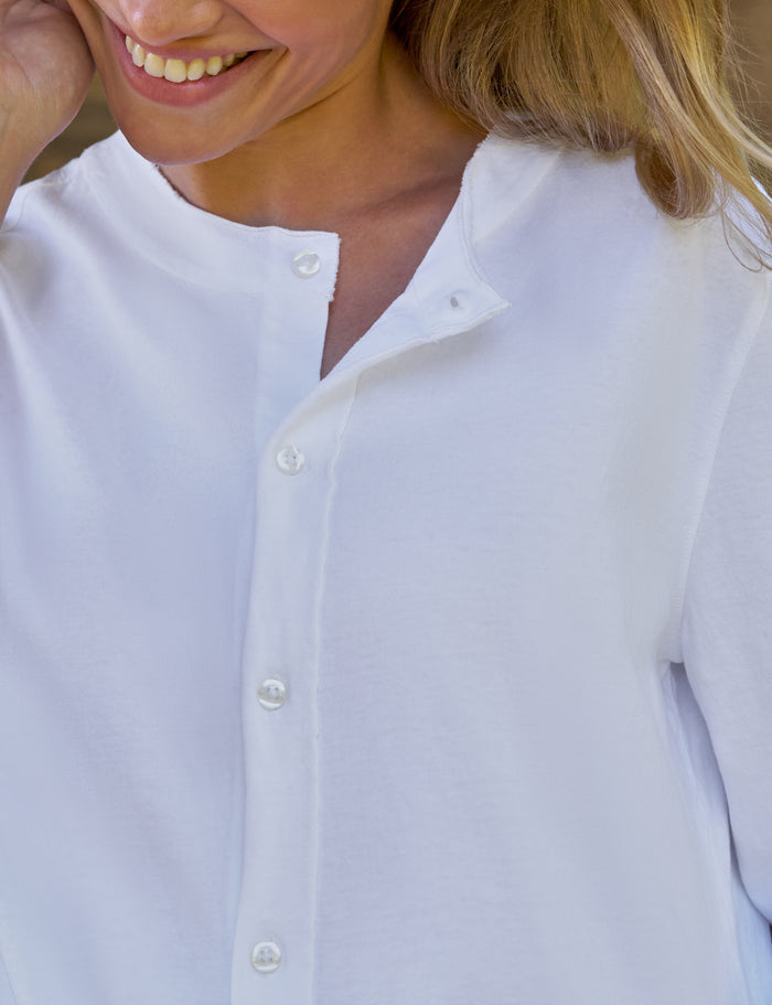 Close-up of a woman wearing a white long-sleeve button-front top with a split neckline and white buttons.