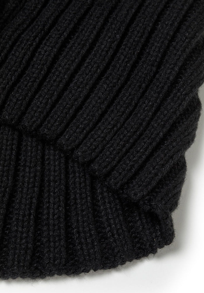 Close-up of a black knitted beanie with ribbed texture and a faux fur pom pom.