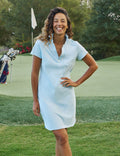 Woman in a light blue dress standing on a golf course with a golf club and flag in the background.