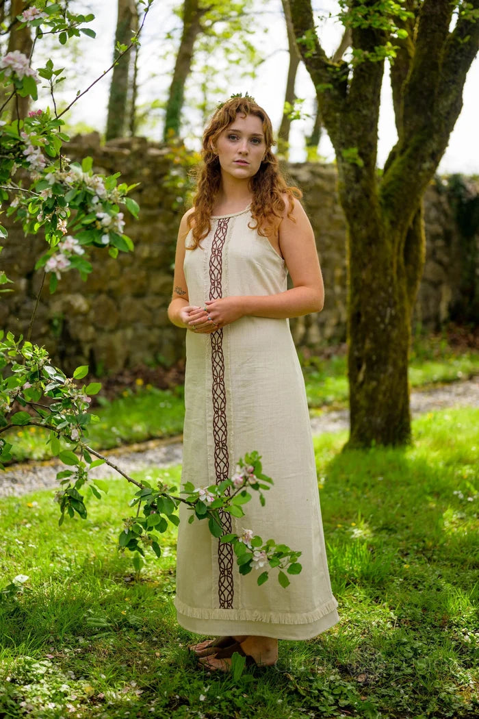 Light Celtic maxi dress in natural cream with central Celtic knotwork panel and fringe hem, shown in a blossom garden designed by Celtic Fusion