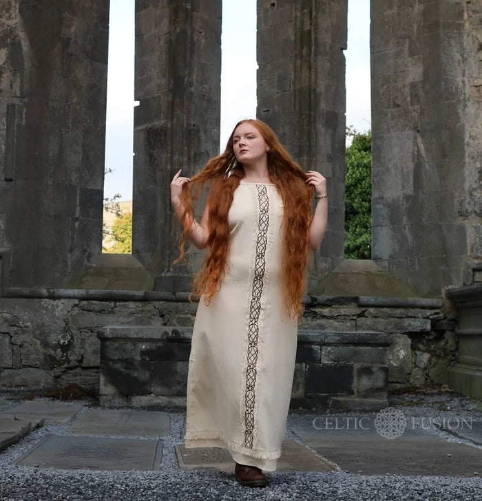 Cream sleeveless Celtic dress with long rope tie back and soft fringe hem photographed at historic stone ruins.