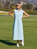 Woman in a light blue dress standing on a grassy field with mountains in the background