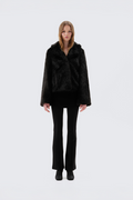 Black faux fur jacket with notch lapel and cropped fit, worn open over a black top and flared trousers, front view