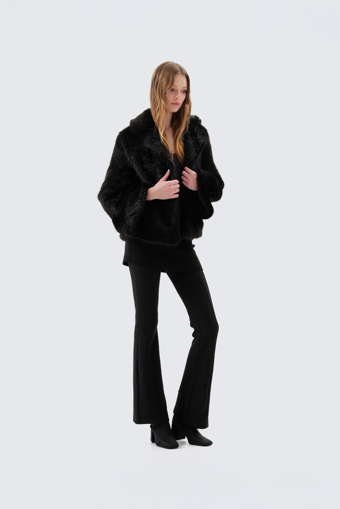 Black faux fur jacket with notch lapel and cropped fit, worn open over a black top and flared trousers
