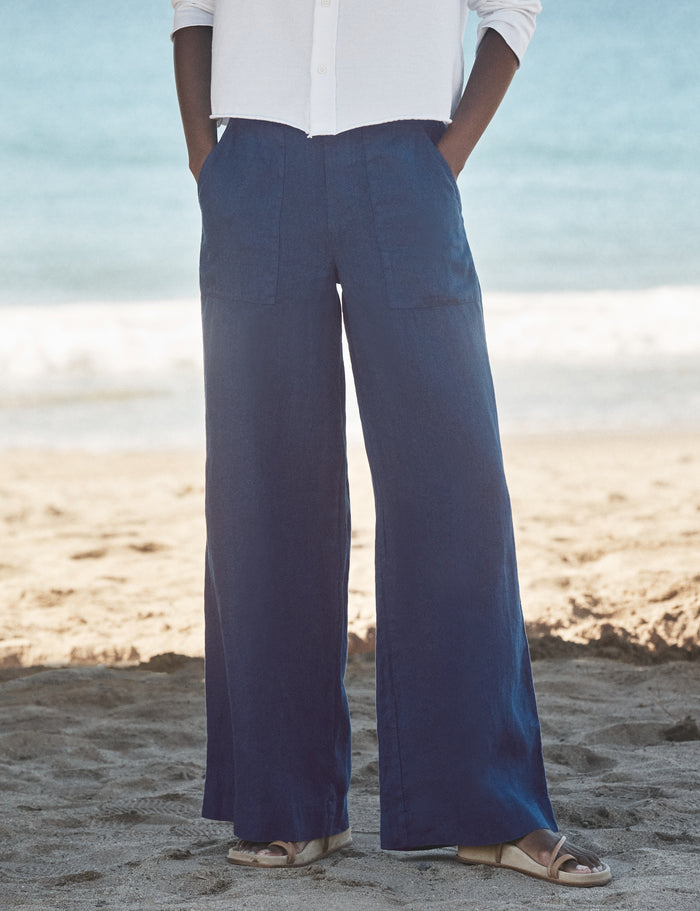 Person wearing blue wide-leg pants and a white shirt on a beach.