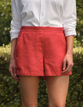 Person wearing red shorts and a white shirt standing on grass with a hedge in the background