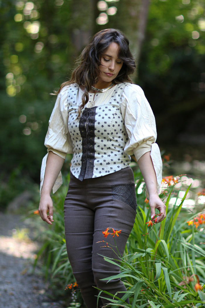 Folklore leaf print lace-up bodice worn over a cream blouse in a woodland garden setting.