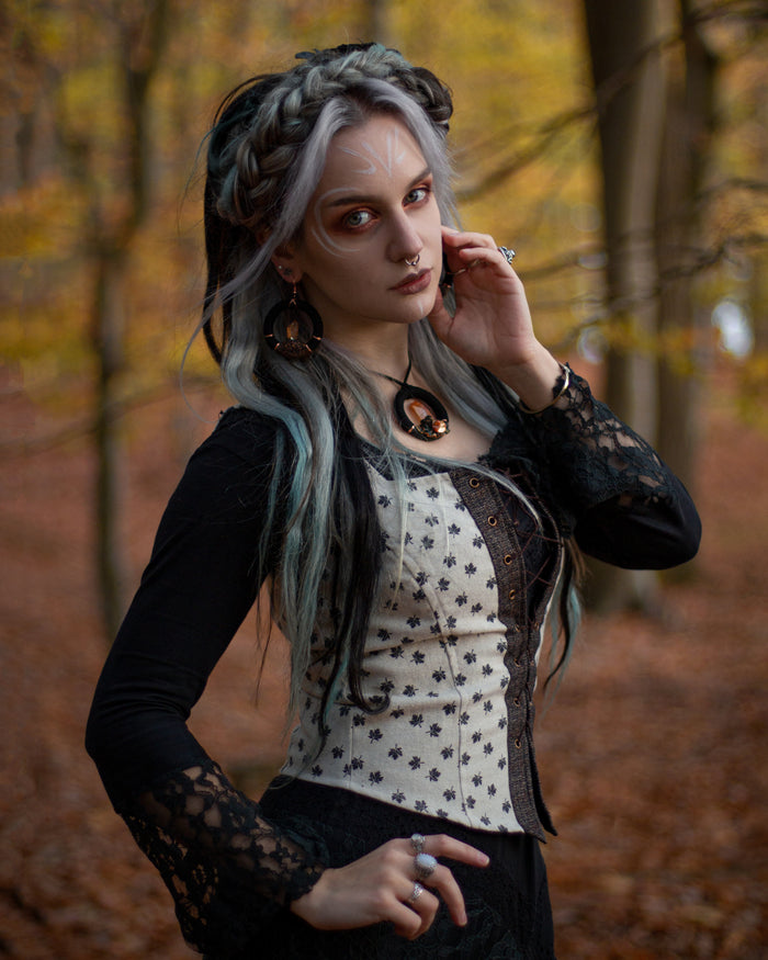 Cream folklore corset top showing the curved fitted shape, pointed hem and dark maple leaf pattern.