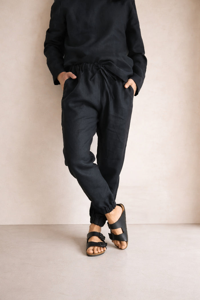 Person wearing black pants and sandals against a beige background