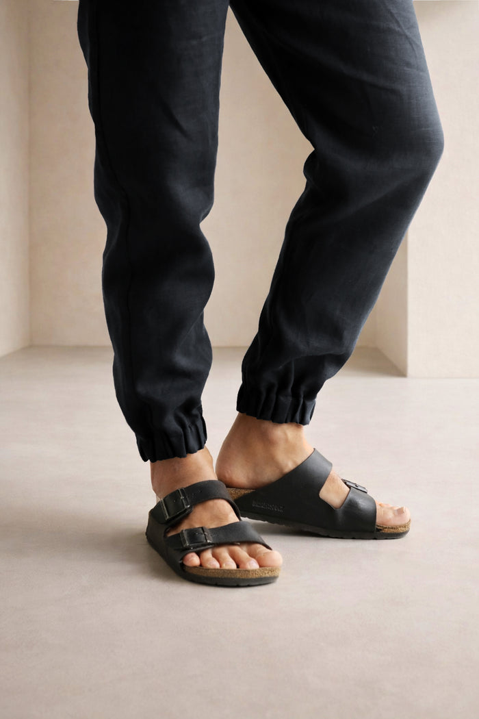 Person wearing black sandals and pants on a neutral background