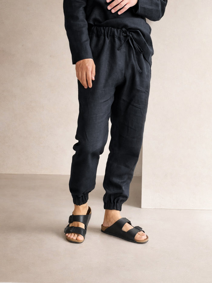 Person wearing black jogger pants and sandals on a neutral background