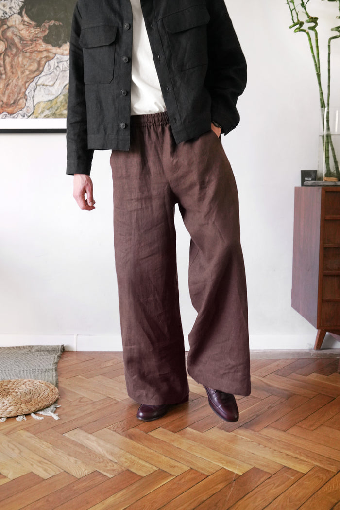 Person wearing a dark jacket and brown wide-leg pants standing in a room with wooden flooring.