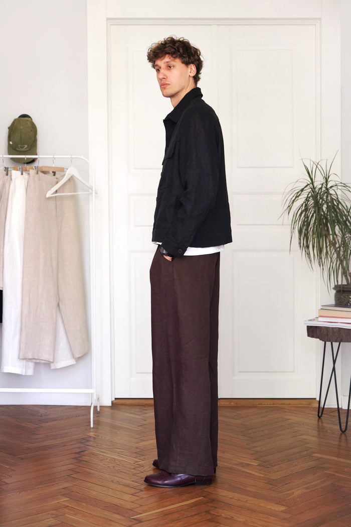 Man standing in a room with white walls, wooden floor, and clothing on a rack.