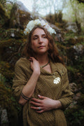 Folk style wool blend shawl with fringe edge and brass oak leaf brooch, worn as a rustic woodland wrap in a mossy forest setting