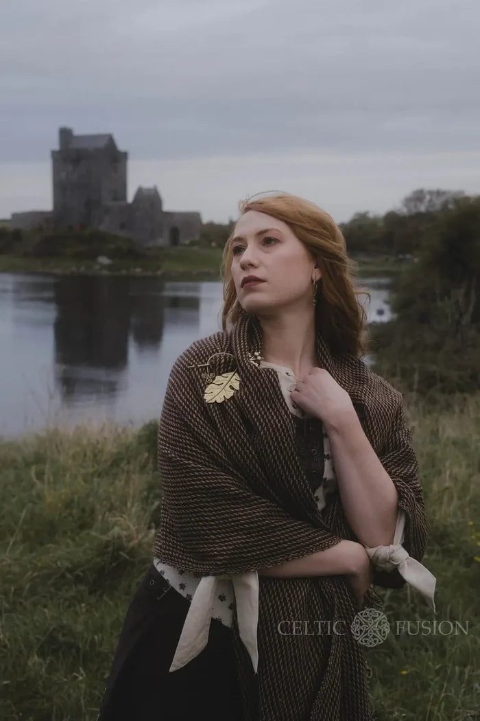 Oak leaf brooch and handwoven shawl styled as an Irish folklore wrap beside a lake with castle backdrop