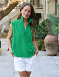 Woman wearing a green sleeveless top and white shorts standing outdoors.
