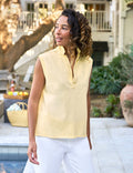 Woman wearing a yellow sleeveless top and white pants standing outdoors.