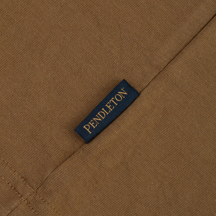 Close-up of a brown woven fabric with a small dark navy label stitched on it, printed with the brand name PENDLETON in gold lettering.