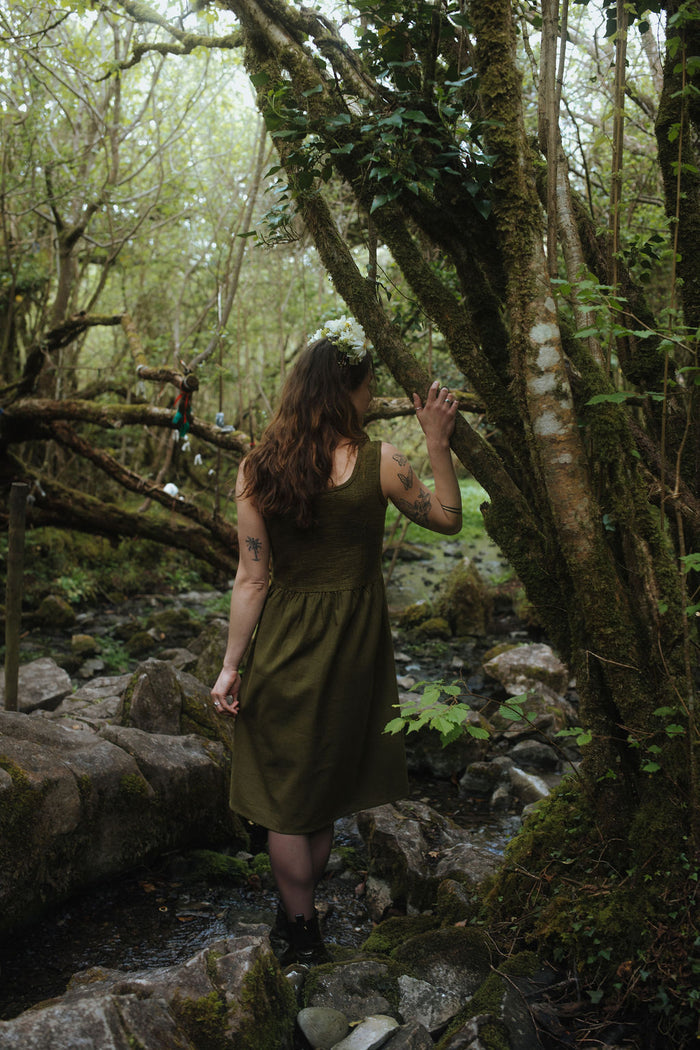 Back view of Rosemary Green Corset Dress, a dark green folklore dress and layering dress in a mossy forest stream