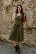 Green Corset Dress styled as a dark green folklore dress with pockets, layered over a cream blouse against a stone wall.