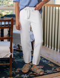 Person wearing white pants and a blue shirt standing in a room with wooden furniture and a floral rug.