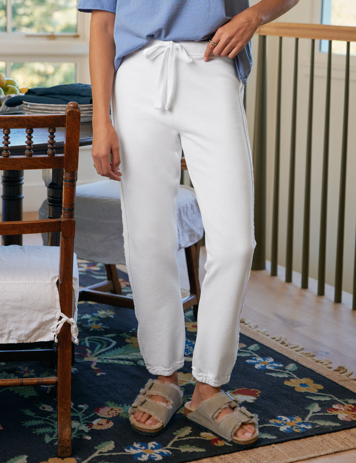 Person wearing white pants and a blue shirt standing in a room with wooden furniture and a floral rug.