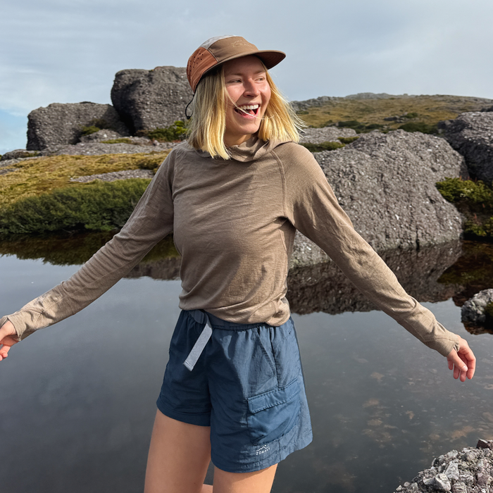 Woman standing by a body of water with rocks and sky in the background