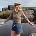 Woman standing by a body of water with rocks and sky in the background